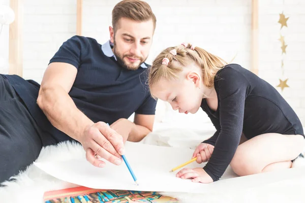 Un joven padre y su hija yacen en el suelo y dibujan con lápices de colores . — Foto de Stock