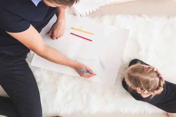 Un joven padre y su hija yacen en el suelo y dibujan con lápices de colores . — Foto de Stock