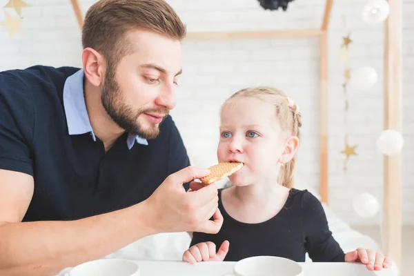 Linda niña y su padre beben té con galletas en casa . — Foto de Stock