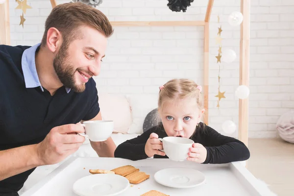 可爱的小女孩和她的父亲喝茶饼干在家里. — 图库照片
