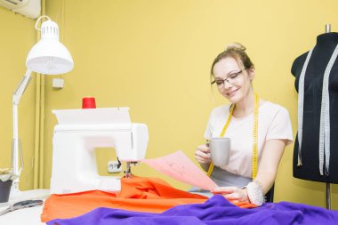 Dikiş atölyesi. Terzi iş başında. Dikiş makinesi ile renkli bir arka plan üzerine çalışan genç kadın