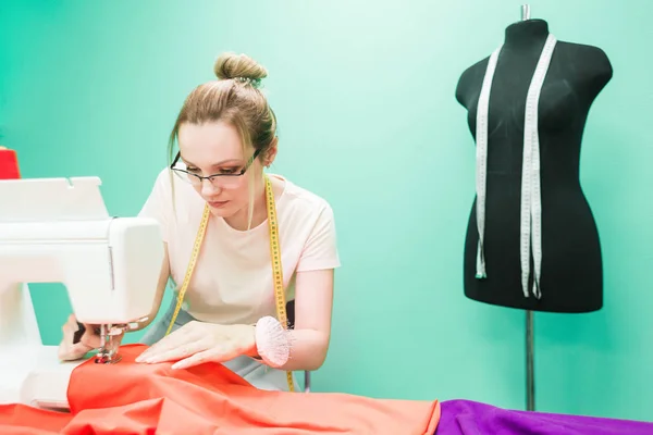 Workshop naaien. Naaister op het werk. Jonge vrouw werken met naaimachine op een gekleurde achtergrond — Stockfoto