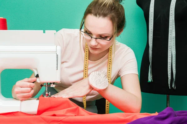 Dikiş atölyesi. Terzi iş başında. Dikiş makinesi ile renkli bir arka plan üzerine çalışan genç kadın