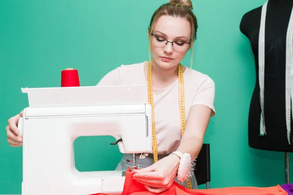 Sewing workshop. Seamstress at work. Young woman working with sewing machine on a colored background