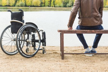 Genç bir adam onun tekerlekli sandalye yanında gölün, bir bankta oturur.