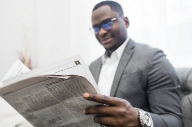 Kanepede otururken bir gazete okuyor gri takım elbiseli Genç Afrikalı-Amerikalı işadamı.