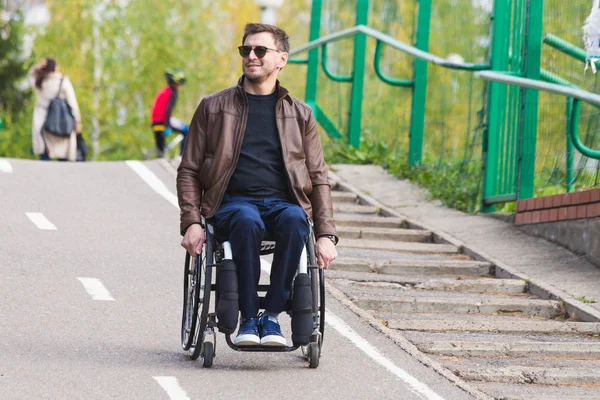 Een jonge man in een rolstoel rijdt langs de weg van park. — Stockfoto