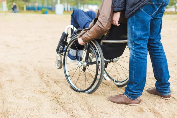 Giovane sulla sedia a rotelle con il suo assistente in una passeggiata nel parco . — Foto Stock