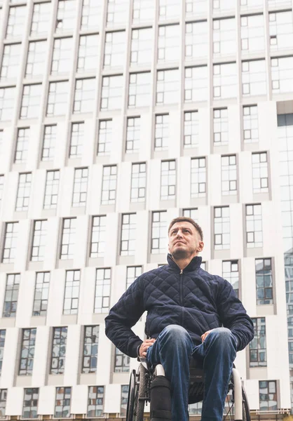 Jonge man in een rolstoel tegen de achtergrond van een moderne hoogbouw-gebouw. — Stockfoto