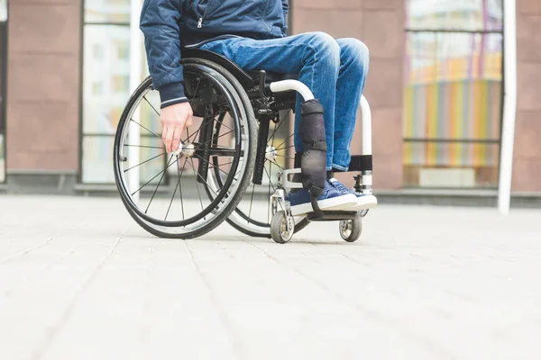 Νεαρός άνδρας σε μια αναπηρική καρέκλα με φόντο ένα μοντέρνο πολυόροφο κτήριο. — Φωτογραφία Αρχείου