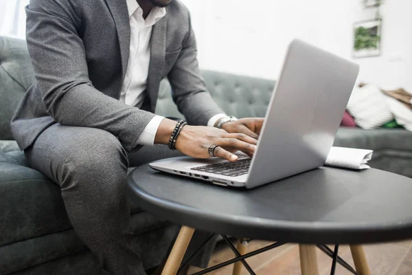 Jeune homme d'affaires afro-américain en costume gris travaillant derrière un ordinateur portable . — Photo