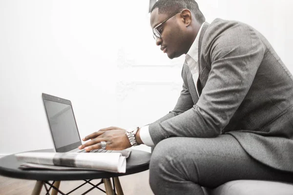Joven hombre de negocios afroamericano en un traje gris que trabaja detrás de una computadora portátil . —  Fotos de Stock