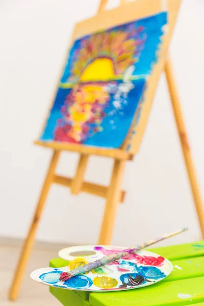 wooden easel in the drawing class with drawings of children. foreground palette. Art class.