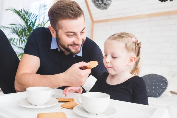 Linda niña y su padre beben té con galletas en casa . — Foto de Stock