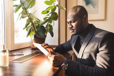 Kafede tablet ile genç yakışıklı koyu tenli işadamı.