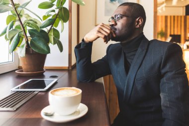 Genç, esmer, yakışıklı iş adamı bir kafede kahve içiyor..