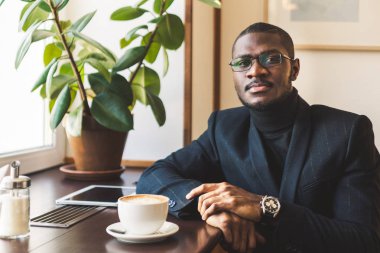 Genç, esmer, yakışıklı iş adamı bir kafede kahve içiyor..