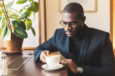 Genç, esmer, yakışıklı iş adamı bir kafede kahve içiyor..