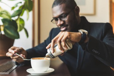 Genç, esmer, yakışıklı iş adamı bir kafede kahve içiyor..