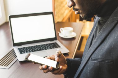 Bir fincan çay ile bir dizüstü bilgisayar arkasında çalışan bir kafede genç yakışıklı koyu tenli işadamı.