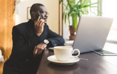 Bir kafede bir çay ile bir cep telefonu konuşurken genç yakışıklı koyu tenli işadamı.