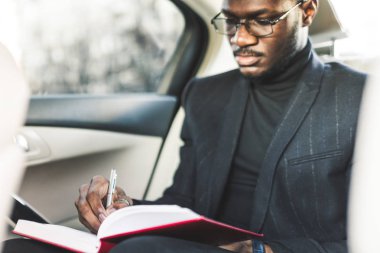 Bir takım elbiseli Genç bir iş adamı bir defter ile pahalı bir arabanın arka koltukta oturuyor. İş görüşmeleri.