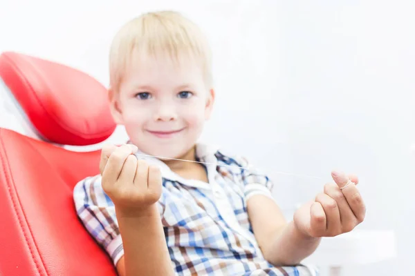 Dental clinic. Reception, examination of the patient. Teeth care. A little boy with dental floss sits in a dental chair. Oral hygiene concept