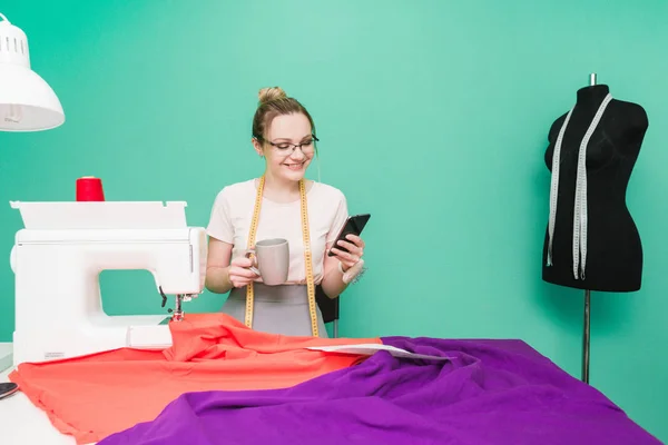 Workshop naaien. Naaister op het werk. Jonge vrouw werken met naaimachine op een gekleurde achtergrond — Stockfoto