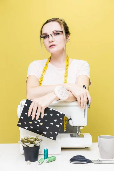 Nähwerkstatt. Näherin bei der Arbeit. Porträt einer jungen Schneiderin mit Notizbuch auf farbigem Hintergrund. — Stockfoto