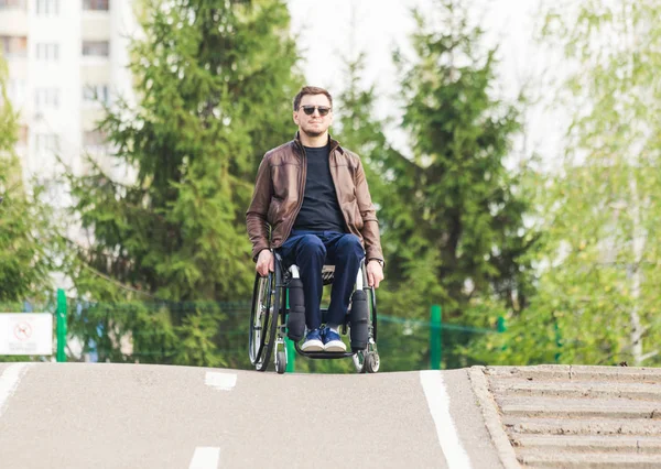 Een jonge man in een rolstoel rijdt langs de weg van park. — Stockfoto