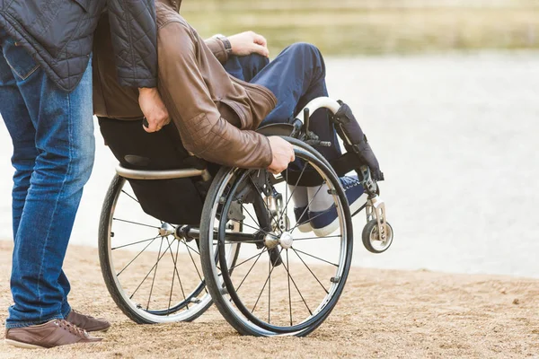 Νεαρός άνδρας σε αναπηρικό καρότσι με τον Βοηθό του σε μια βόλτα στο πάρκο. — Φωτογραφία Αρχείου