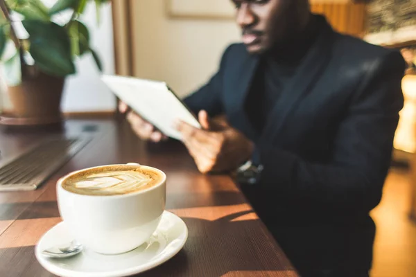 Ung vacker mörkhyade affärs man med tablett i kafé med en kopp kaffe. — Stockfoto