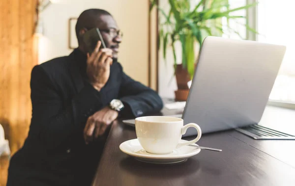 Joven hombre de negocios guapo de piel oscura en un café hablando en un teléfono celular con una taza de té . —  Fotos de Stock
