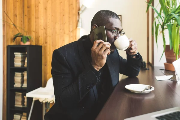 Ung vacker mörkhyade affärs man i ett kafé som pratar på en mobil telefon med en kopp te. — Stockfoto