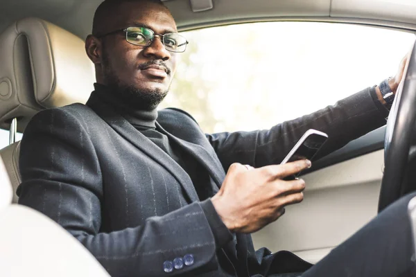 Egy üzletember vezetői egy drága autót tart a mobil telefon a kezében. Elhamarkodott élet. — Stock Fotó