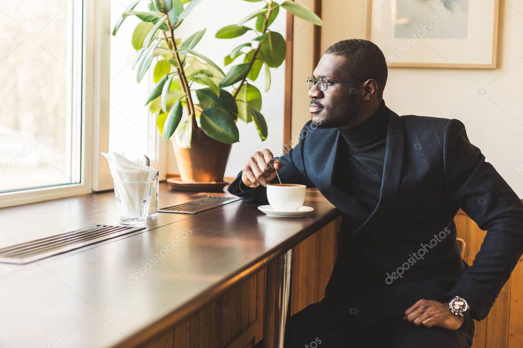 Young handsome dark-skinned businessman drinks coffee in a cafe.