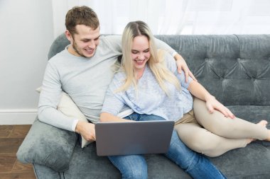 Genç güzel çift kanepede istirahat ve oturma odasında bir laptop online video izlerken.