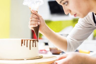 Bir şekerlemeler ahşap bir stand üzerinde beyaz krem bisküvi kek üzerine bir pasta torbası sıvı çikolata sıkır. Ev yapımı pasta kavramı, yemek pastaları.