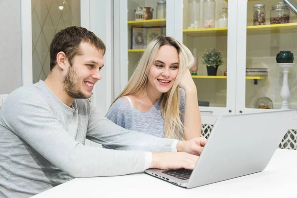 Pareja joven sentada por la mañana en la cocina y utilizando el ordenador portátil. Concepto de compras online. Cocina moderna en el fondo . — Foto de Stock