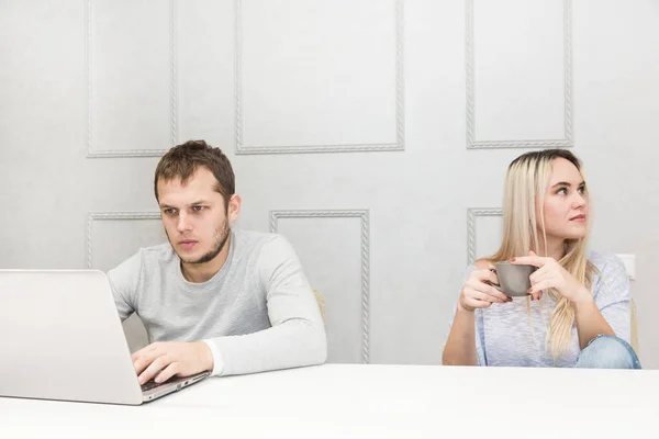 Молодая пара завтракает. Мужчина работает за ноутбуком, женщина скучает смотрит в сторону . — стоковое фото