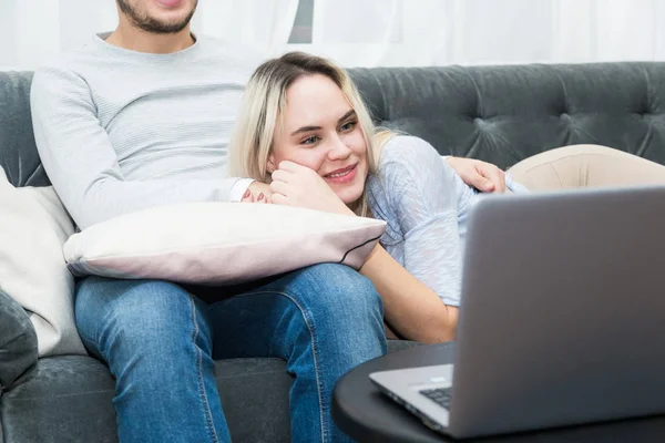 Jovem casal bonito descansando no sofá e assistindo vídeo on-line de um laptop na sala de estar . — Fotografia de Stock