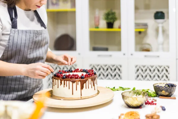 糖果装饰与浆果饼干蛋糕与白奶油和巧克力。蛋糕站在白色桌子上的木制支架上。自制糕点、烹饪蛋糕的概念. — 图库照片