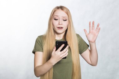 Şaşırtılmış ve endişeli genç bir kadın bir akıllı telefon tutarak, sürpriz bir ifade ile bakıyor.