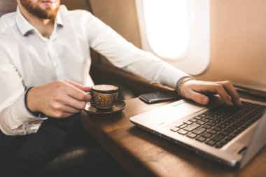 Çekici ve başarılı işadamı kahve içme ve onun özel jet bir sandalyede otururken bir laptop arkasında çalışma.