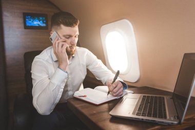 Genç, çekici ve başarılı bir iş adamı özel iş uçağında otururken telefonda konuşuyor ve çalışıyor.
