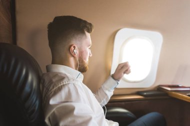 Genç ve başarılı iş adamı dinleniyor ve özel iş uçağının koltuğunda oturmuş müzik dinliyor.