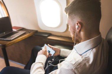 Genç ve başarılı iş adamı dinleniyor ve özel iş uçağının koltuğunda oturmuş müzik dinliyor.