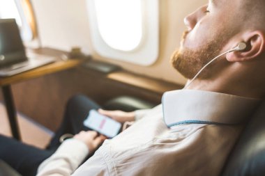 Genç ve başarılı iş adamı dinleniyor ve özel iş uçağının koltuğunda oturmuş müzik dinliyor.