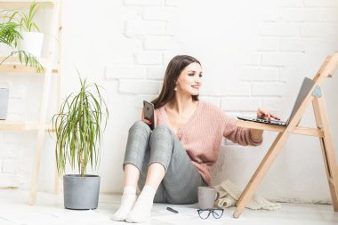 Ev yapımı günlük giysiler içinde mutlu bir kadın parlak bir iç mekanda oturur ve telefon kullanır, kız bir dizüstü bilgisayarda çalışırken ve internette sörf yaparken dinlenir. Rahat serbest çalışma alanı,