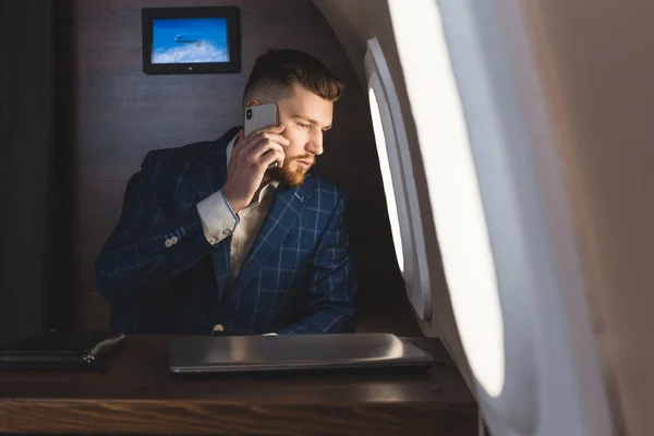 Joven empresario atractivo y exitoso hablando por teléfono y trabajando mientras está sentado en la silla de su avión privado de negocios — Foto de Stock